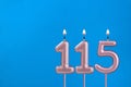 Number 115 - Burning anniversary candle on blue foamy background