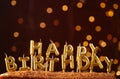 Minimalistic background with golden candles without fire letters in cake close up. Garland of yellow bokeh circles at