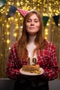 Birthday celebration. Young woman holding a cake with candles celebrating her 18th birthday at home against a decorated Royalty Free Stock Photo