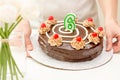 Birthday chocolate cake with candle in the form of number Six in woman hands. Homemade cake decorated with chocolate cream and Royalty Free Stock Photo