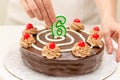 Birthday chocolate cake. Woman hands decorating cake with candle in the form of number Six Royalty Free Stock Photo