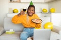 Birthday concept. Joyful black woman having online b-day party, holding pie with burning candle and glass of wine Royalty Free Stock Photo