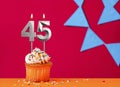 Birthday cupcake with candle number 45 on a red background with blue pennants