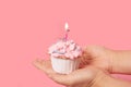 Birthday cupcake with candle and party hat on pink background.