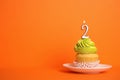 Birthday cupcake with number two candle in saucer on orange background Royalty Free Stock Photo