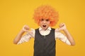 Birthday kids party. Funny kid in curly clown wig isolated on yellow background. Angry teenager girl, upset and unhappy Royalty Free Stock Photo