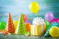 Birthday party background with gift box, colorful balloons, confetti, carnival cap and streamer. Holiday supplies on blue table Royalty Free Stock Photo