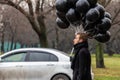 Birthday is a sad holiday concept. A young blonde man wearing black scarf and coat guy holding black balloons and smoking. Royalty Free Stock Photo