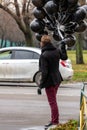 Birthday is a sad holiday concept. A young blonde man wearing black scarf and coat holding black balloons going down street, back Royalty Free Stock Photo