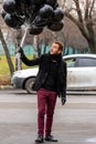 Birthday is a sad holiday concept. A young blonde man wearing black scarf and coat holding black balloons going down street, front Royalty Free Stock Photo