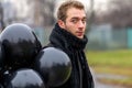 Birthday is a sad holiday concept. A young blonde man wearing black scarf and coat holding black balloons going down street, front Royalty Free Stock Photo