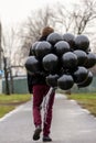 Birthday is a sad holiday concept. A young blonde man wearing black scarf and coat holding black balloons going down street, back Royalty Free Stock Photo