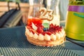 Birthday summer cream cheese cake with gold 23 number candle, fresh red strawberry berries on the table outdoors. Close Royalty Free Stock Photo