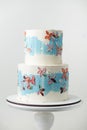 Birthday two tier cake with white chocolate frosting decorated with blue smears and multicolored pastel cream flowers on the white