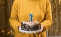 Birthday 3. Woman holding birthday cake with burning candles number 3 against decorated background, close up. Celebrates