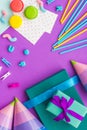 Birthday wrapped gifts and party hats on purple background top view copyspace