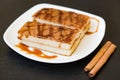 Biscuit cake with caramel syrup on white plate with cinnamon sticks on wooden background, Royalty Free Stock Photo