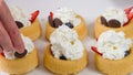 Biscuit cakes with fresh berries, chocolate, and whipped heavy cream. Woman preparing dessert, mini biscuit cups with strawberries