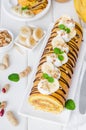 Biscuit or sponge cake roll with peanut butter cream, bananas and chocolate glaze on a white wooden background. Vertical Royalty Free Stock Photo