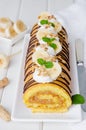 Biscuit or sponge cake roll with peanut butter cream, bananas and chocolate glaze on a white wooden background. Vertical Royalty Free Stock Photo