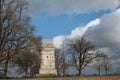 The Bismarck Tower near Augsburg stands between bare trees in February. A cyclist rides past it. The sky is blue with white clouds