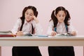 A bit bored schoolgirl twins learning from textbooks, sitting behind the desk Royalty Free Stock Photo