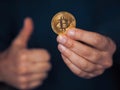 Bit coin on one hand, other hands in thumbs up gesture. Selective focus. Dark blue background. Money and finance concept.