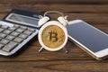 Bitcoin, alarm clock, calculator, smartphone on a wooden background.