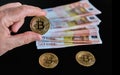 Bitcoin coin held with fingers, together with others, and a set of 50 euro banknotes. Concept of wealth, power, economy. Selective