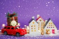 Bitcoin coin on red retro car past houses with fairy lights and snow, Christmas tree with gift boxes on roof. Violet background.