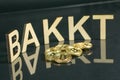 Bitcoin coins in front of bakkt sign made of wood with reflection on the table