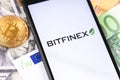 Bitcoin, dollars, euro banknotes and Bitfinex logo of exchange on the screen smartphone