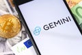 Bitcoin, dollars, euro banknotes and Gemini logo of crypto-exchange on the screen smartphone