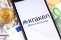 Bitcoin, dollars, euro banknotes and Kraken logo of exchange on the screen smartphone