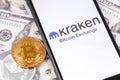 Bitcoin, dollars and Kraken logo of exchange on the screen smartphone