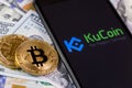 Bitcoin, dollars and KuCoin logo on the screen smartphone
