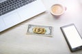 Bitcoin golden coins on a dollar banknotes. Office background. Cup of coffee, white laptop, mobile phone, and money. Money balance Royalty Free Stock Photo