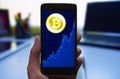 Bitcoin price growth graph. Cryptocurrency Bitcoin symbol and growth chart at the smartphone screen, smartphone in the hand.