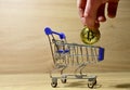 Bitcoin in shopping cart. Man`s hand puts a BTC gold crypto coin in mini shopping trolley. Blockchain and financial technology.