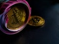 Bitcoin token rests against a rolled stack of banknotes on a dark surface. Royalty Free Stock Photo