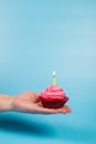 Bithday cupcake in female hand. Cupcake with candle on blue background. Lonely birthday