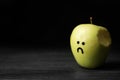 Bitten apple with drawing of unhappy face on table against dark background, space for text. Royalty Free Stock Photo