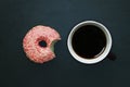 Bitten donut in pink glaze and cup of coffee on dark background, view from above Royalty Free Stock Photo