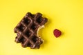 Bitten off chocolate waffle and raspberry, yellow background, top view
