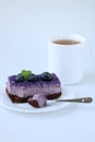 Bitten off purple blueberry mousse cake with blueberry on white plate with teaspoon and cup of tea on white background Royalty Free Stock Photo