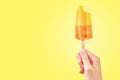 Bitten red frozen fruit ice cream popsicle in woman hand on yellow background Royalty Free Stock Photo