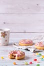 Bitten strawberry donuts with pink icing, colorful sprinkles and jelly beans on wooden background. Sweet pastry party snack. Royalty Free Stock Photo