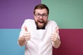 Bizarre bearded man in round glasses makes an approving gesture with hands thumbs up and joyfully looks into the camera