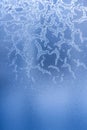 Bizarre frosty pattern of ice crystals on blue frozen winter window.