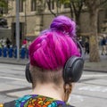 Bizarre hair style of a young woman walking in the city center with headphones on her head